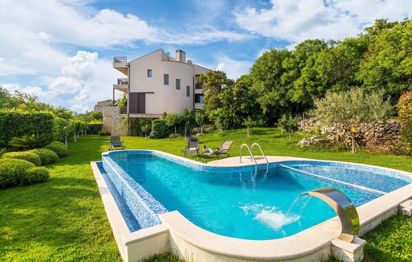Une piscine bordée de pierres, entourée d’une pelouse bien entretenue et d’arbres.