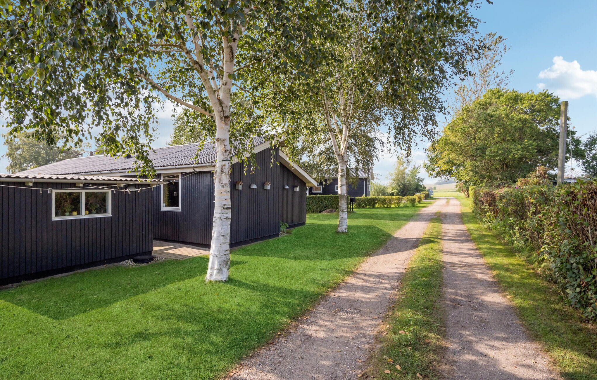 A row of dark wooden cabins with a gravel path leading through a grassy area.