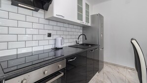 Une cuisine moderne avec des carreaux de céramique blancs disposés en motif métro, un plan de travail noir, un four encastré, une bouilloire et un réfrigérateur.
