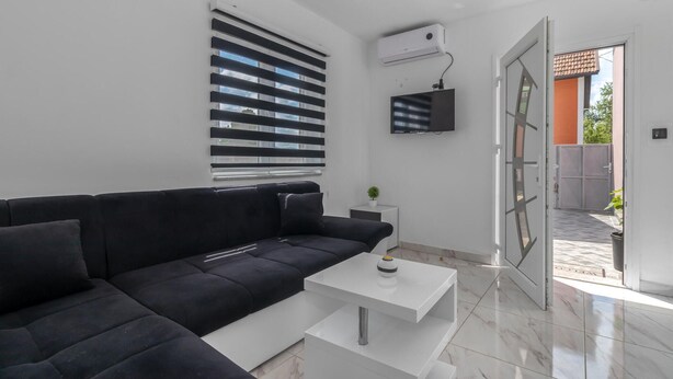 Un salon moderne avec un canapé noir, une table basse blanche et un téléviseur fixé au mur.