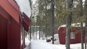 A snow-covered path leading to a red cabin surrounded by trees.