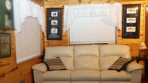 A beige leather sofa with two pillows, a framed fish picture on the wall, and a clock on the left.