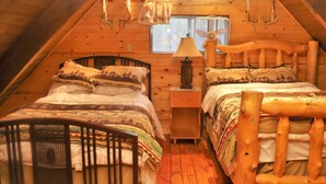 A cozy attic bedroom with two wooden beds, a small table, and a window with a fan.