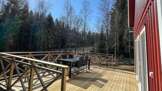 Eine Holzterrasse mit Tisch und Stühlen, umgeben von einem Geländer, mit Blick auf bewaldetes Gebiet.