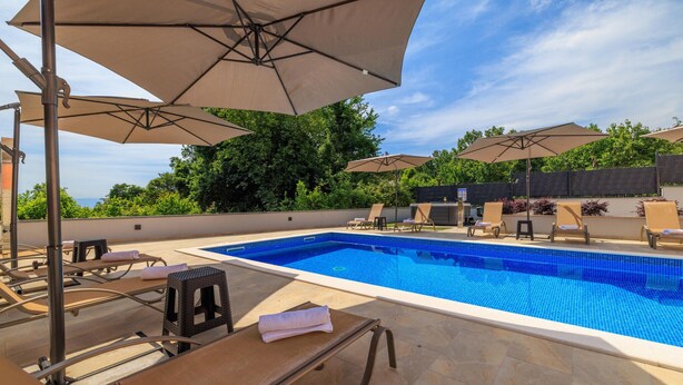 A swimming pool with lounge chairs and umbrellas, surrounded by greenery and a clear sky. - Amazing apartment in Opric with swimming pool (Opric)