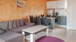 Una habitación moderna con un sofá gris, una mesa de comedor con sillas, una zona de cocina con armarios y una alfombra morada.