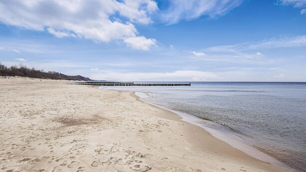 Una playa con un muelle que se adentra en el agua, orilla arenosa y cielo despejado.