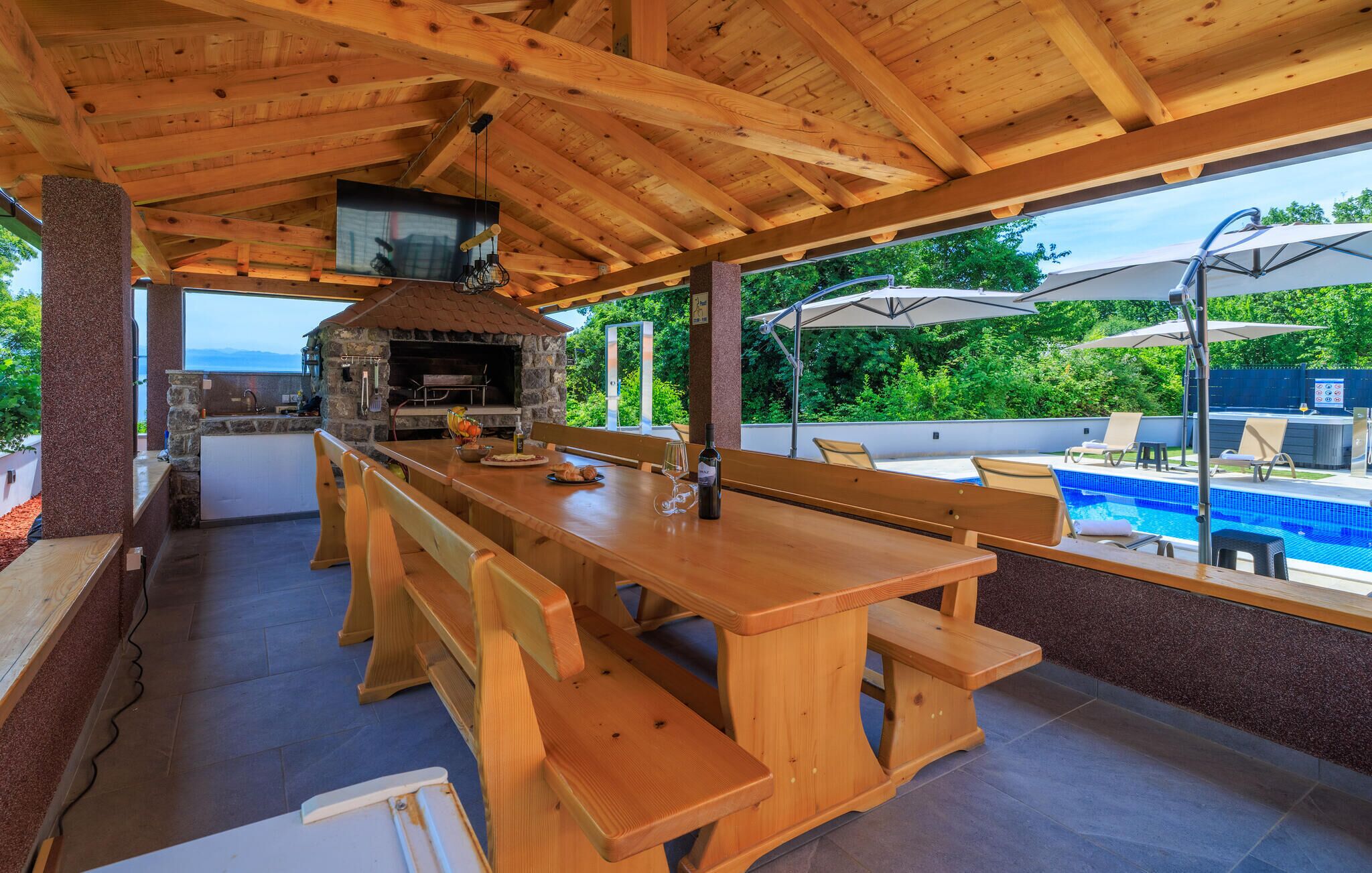 An outdoor kitchen with a stone oven, wooden benches, and a poolside area with umbrellas.