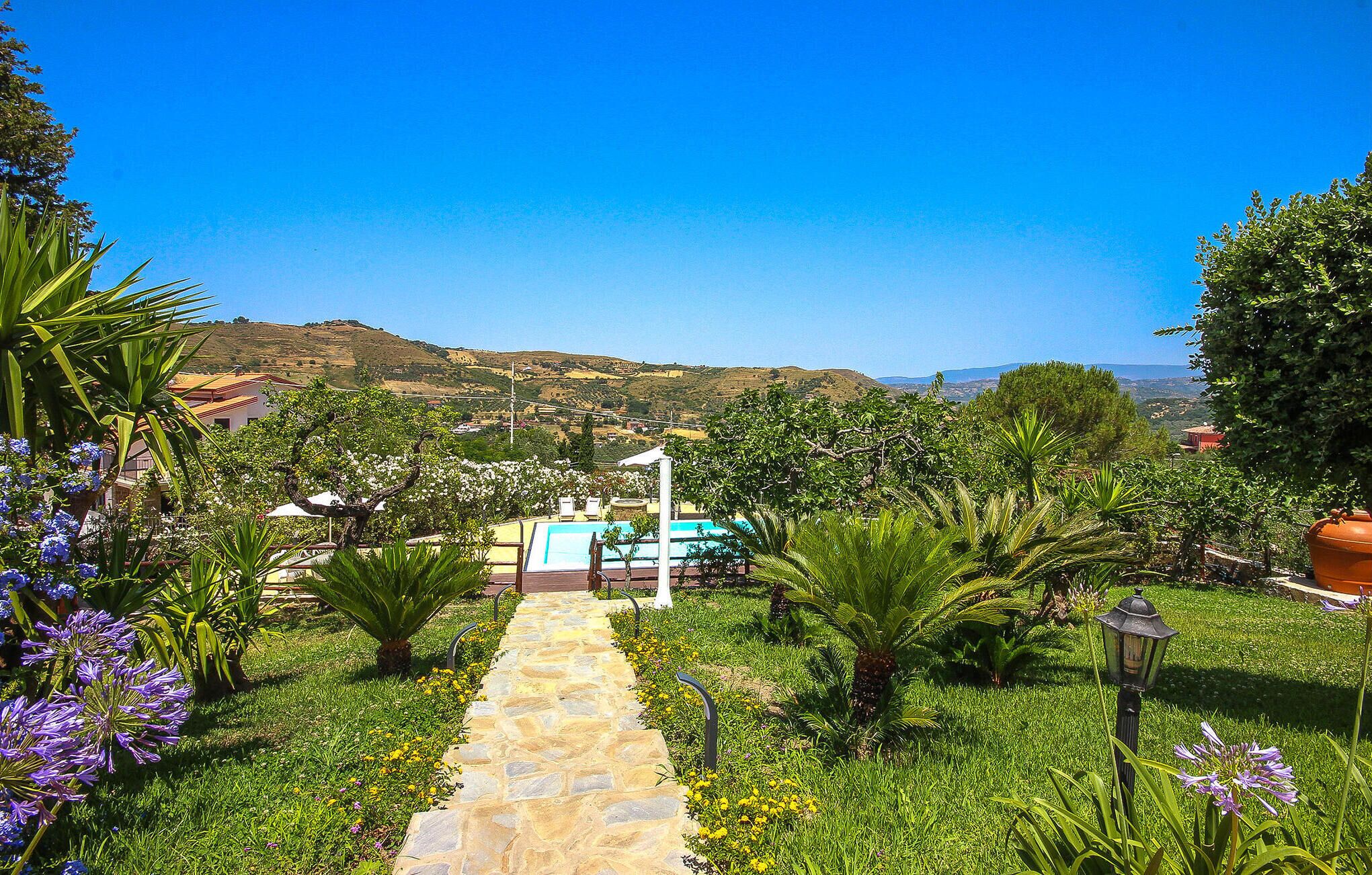 A stone pathway leading to a pool area surrounded by lush greenery and flowering plants.