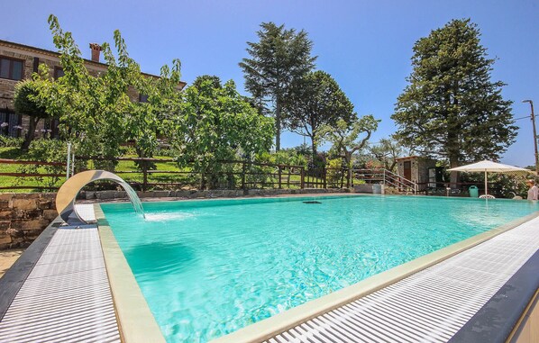 Relax by the serene pool surrounded by lush greenery and a stone wall, with lounge chairs and a soothing waterfall feature.