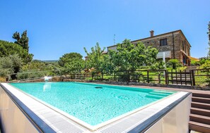 Relax by the pool surrounded by lush greenery and a traditional stone building.