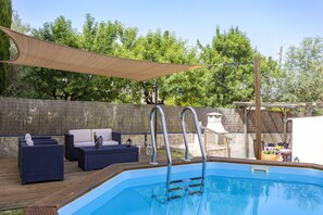 Una piscina con cubierta de madera, sillas de descanso y una zona sombreada con una vela.