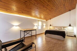 Un dormitorio con techo de madera, una cama, mesitas de noche y luces fijadas en la pared.