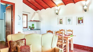 A cozy living room with a sofa, a dining table set for four, and a kitchen in the background.