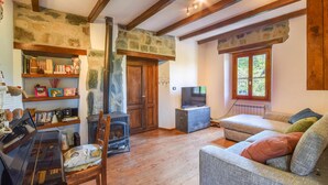 Un salon chaleureux avec une cheminée, des poutres en bois, des murs en pierre, un téléviseur et un piano.