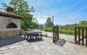 A stone patio with a table and chairs, a brick oven, and a wooden gate. - 4 bedroom stunning home in Tiglieto (Tiglieto)