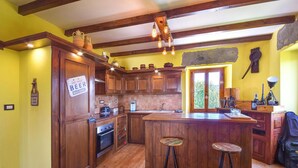 Une cuisine avec des meubles en bois, un îlot central doté de tabourets, un mur en pierre et une enseigne indiquant : « Bière bien fraîche à vendre ici ».