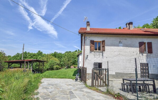 A stone house with a red-tiled roof, a wooden door, and a small garden area with a stone pathway leading to a wooden bench and table. - 4 bedroom stunning home in Tiglieto (Tiglieto)