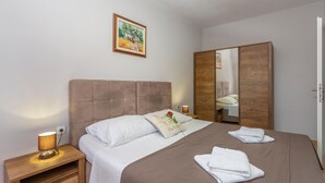 Un letto ben rifatto con lenzuola bianche, un comodino in legno con una lampada, un quadro incorniciato appeso al muro e un armadio in legno.