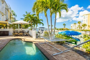 A pool area with a hammock, lounge chairs, and umbrellas.