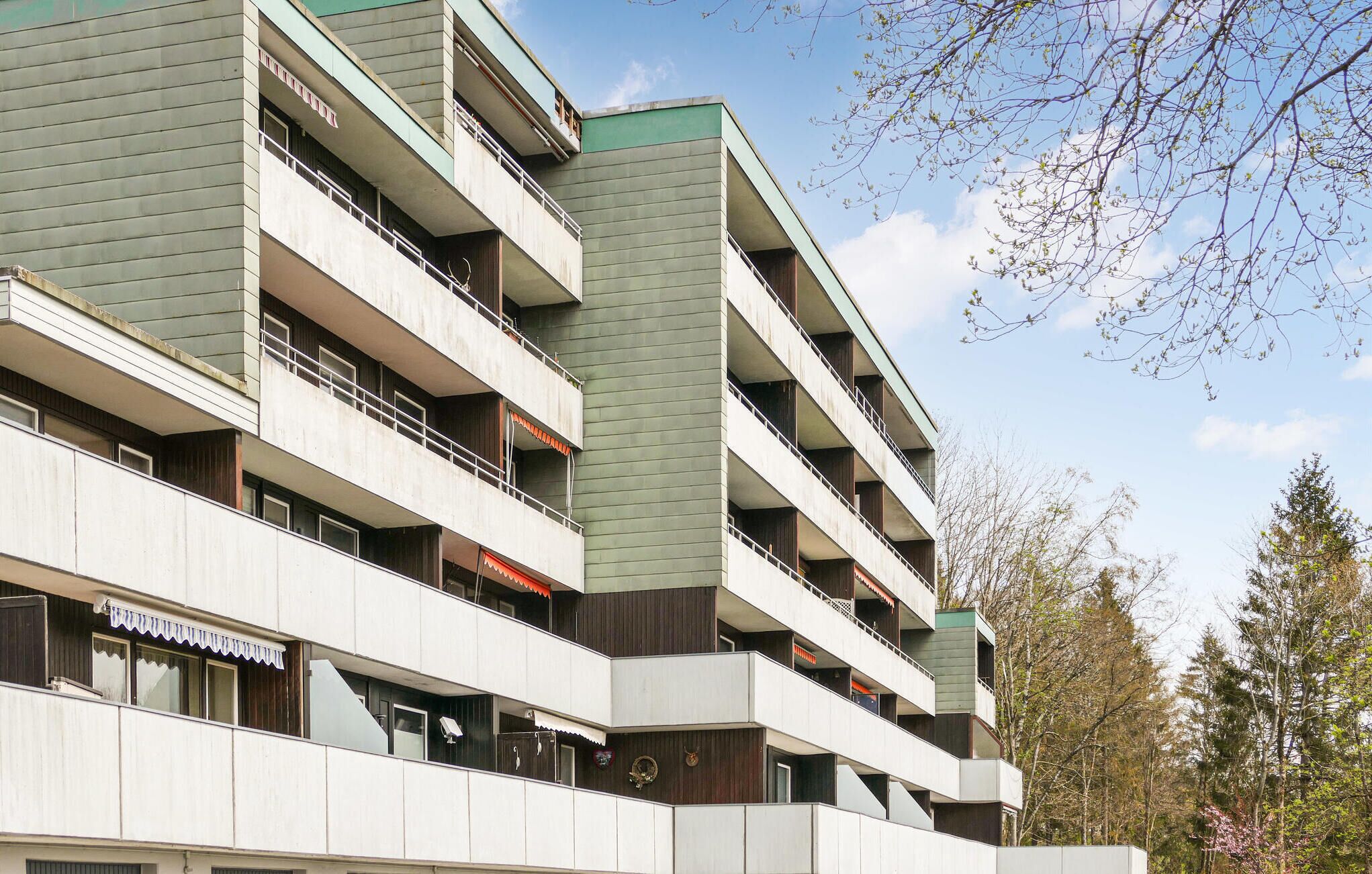 A multi-story building with balconies, a flat roof, and a mix of concrete and wood paneling.