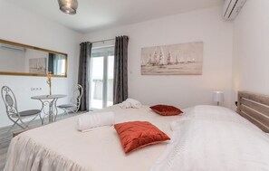Une chambre d’hôtel avec un lit, une chaise, une petite table, un tableau et une fenêtre avec des rideaux.