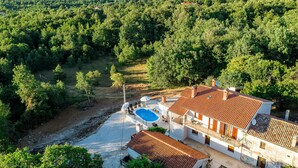 Een villa met een zwembad, omgeven door dicht bos en heuvels op de achtergrond.
