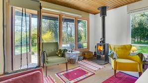 A cozy room with a fireplace, a green armchair, a yellow armchair, and large windows overlooking a garden. - Awesome home in Fårevejle with kitchen (Fårevejle)