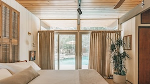 Un dormitorio con una cama grande, puertas de cristal correderas que dan a una zona de piscina y una planta en maceta.