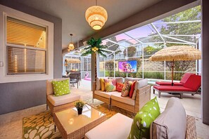 A sunlit patio with wicker furniture, a glass enclosure, and a television screen.