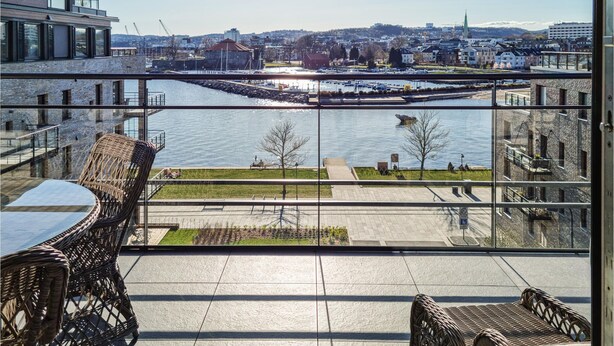 Un balcon avec des fauteuils en osier et une table, donnant sur une rivière, avec une vue sur la ville en arrière-plan.