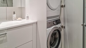 Une petite buanderie équipée d’un lave-linge, d’un évier et de produits de toilette.