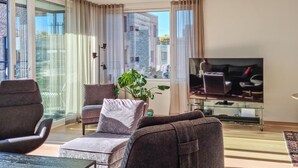 Un salon moderne doté d’un grand téléviseur, de sièges confortables et offrant une vue sur la ville.
