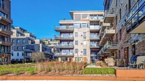 Un immeuble d’appartements moderne doté de nombreux balcons, d’une cour intérieure agrémentée de plantes et surplombé d’un ciel d’un bleu éclatant.