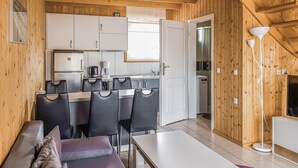 A modern kitchen with white cabinets, a coffee maker, and a refrigerator. There is a dining area with a table and chairs, and a sofa.