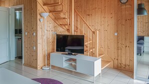 A modern living room with a flat-screen TV on a white console, wooden walls, a staircase, and a visible clock.