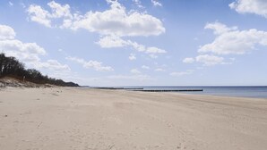 A wide sandy beach with a clear sky and a wooden pier extending into the water.