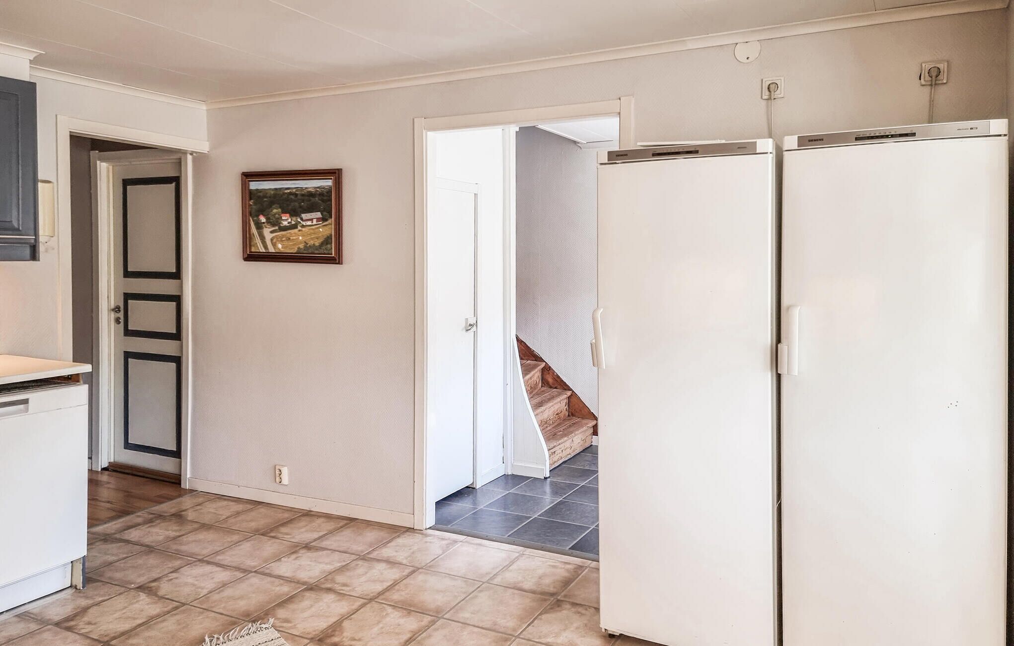 Une cuisine équipée d’un réfrigérateur, d’une porte ornée d’un tableau et d’un escalier menant à un palier.