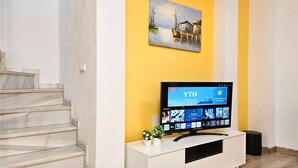 Uma sala de estar moderna com uma televisão de tela plana sobre um móvel branco, um quadro acima da TV e uma escada à esquerda.