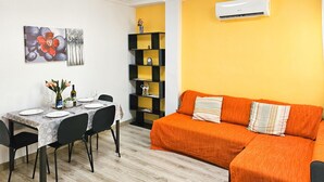 Uma área de refeições com uma mesa posta para dois, uma estante preta e um sofá laranja.