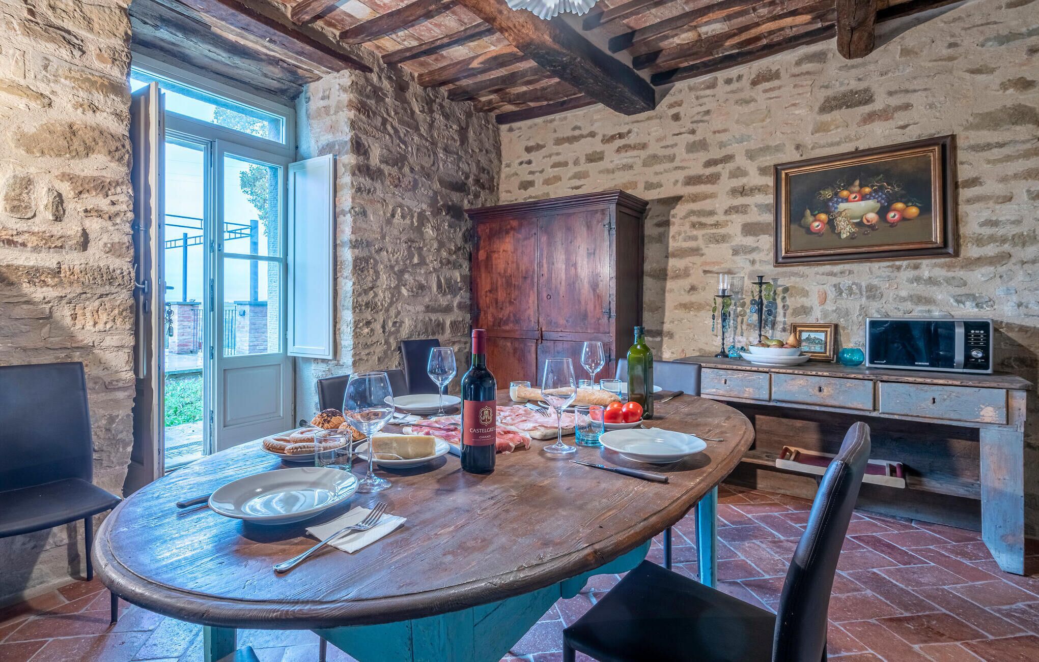 A rustic dining area with a stone wall, wooden beams, and a large wooden table set for a meal.