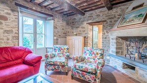 A rustic room with stone walls, a red sofa, floral armchairs, and a fireplace.