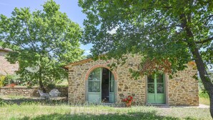 A stone building with an arched entrance, a green door, and a small porch area with a chair and a potted plant.