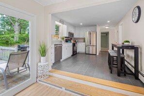 A modern kitchen with white cabinets, stainless steel appliances, and a large window overlooking a deck. - 1.2 miles from the beach & Private Bike Trail Access - Hillside Hideaway (Harwich)