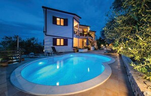 Une maison à deux étages avec une piscine, du mobilier d’extérieur et un balcon bien éclairé.