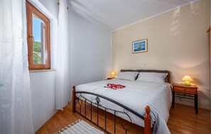 Une chambre à coucher avec un lit, deux tables de chevet avec des lampes, une fenêtre avec des rideaux, un tableau encadré au mur et un plancher en bois.