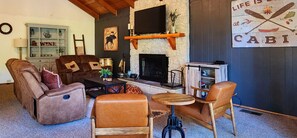 A cozy living room with leather sofas, a fireplace, and rustic decor. - Fenced lot, 1/4 Acre Lot & EV Charger (Running Springs)