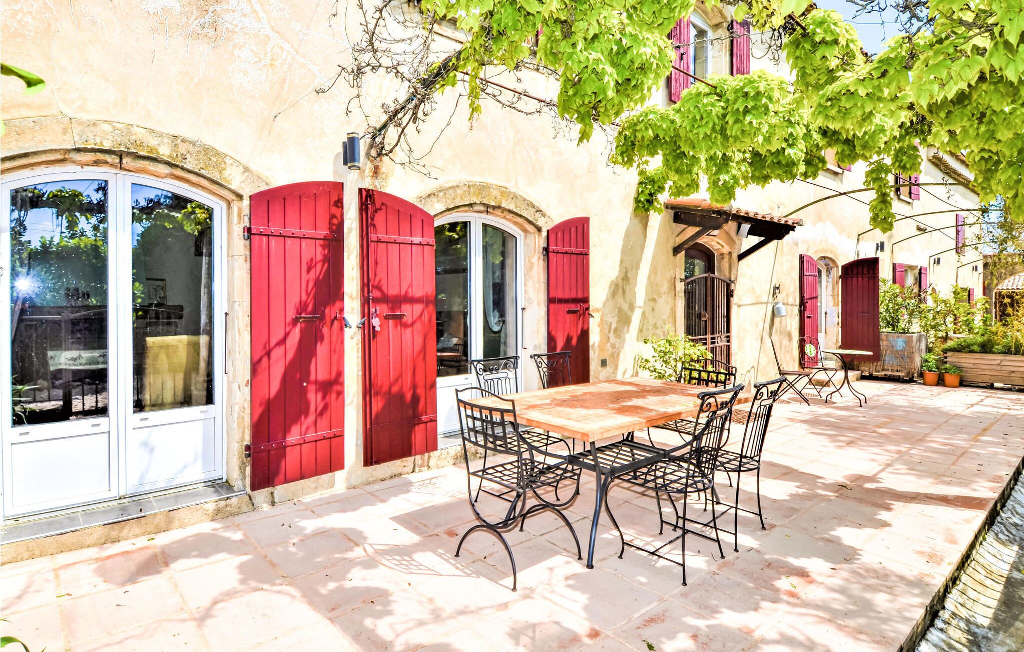 Ein Innenhof mit Holztisch und -stühlen, roten Türen und einer mit Pflanzen bewachsenen Pergola.