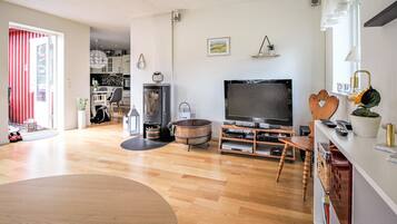A living room with a wooden floor, a TV, a fireplace, and a dining area with a table and chairs.