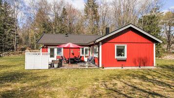 A red wooden cabin with a porch, a flag, and outdoor furniture.